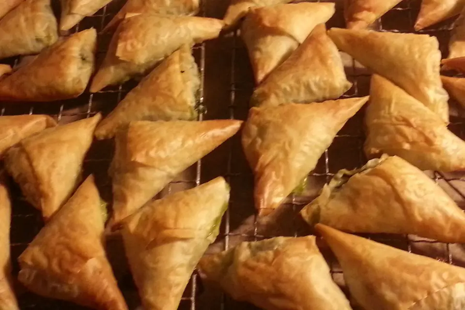 Triangular spinach börek pastries on a wire rack