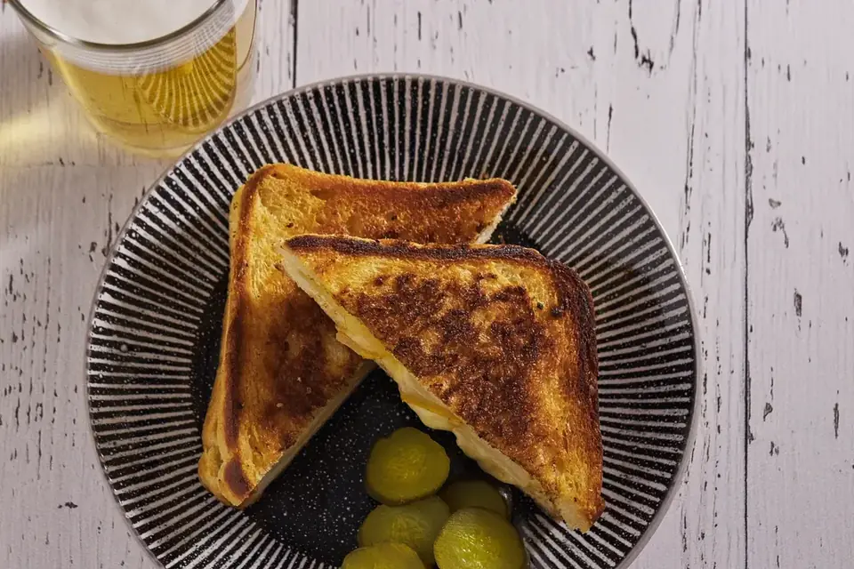 A cheese toastie cut into triangles with pickles on a plate