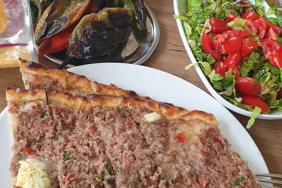 Ground meat pide with roasted peppers and salad on a plate