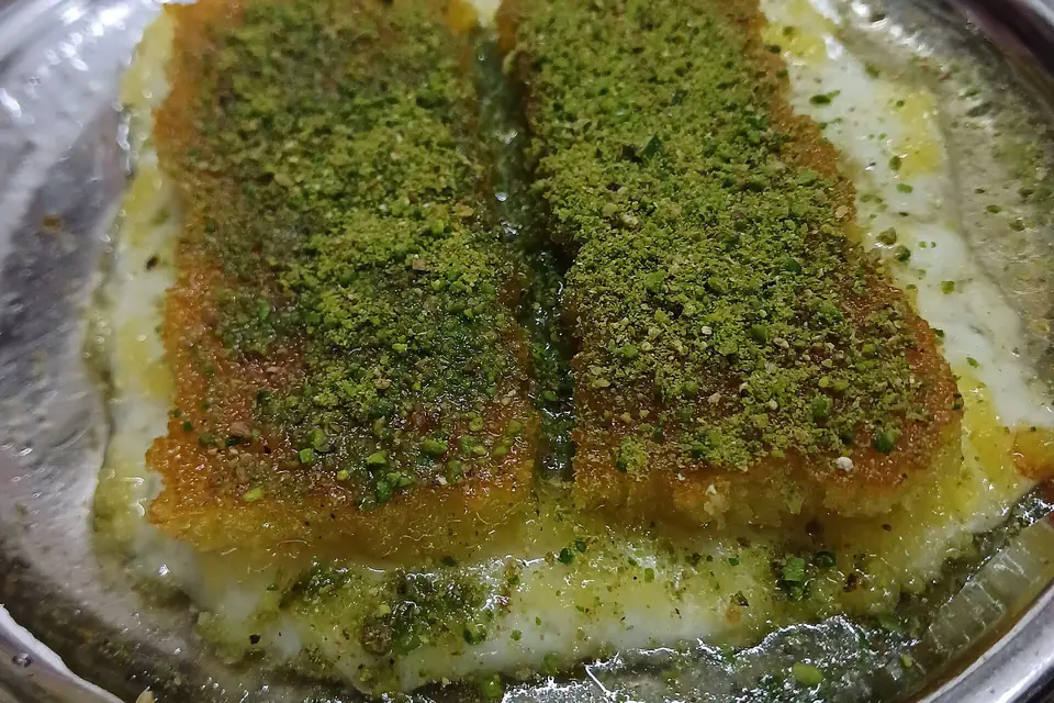 Künefe topped with pistachios on a metal plate
