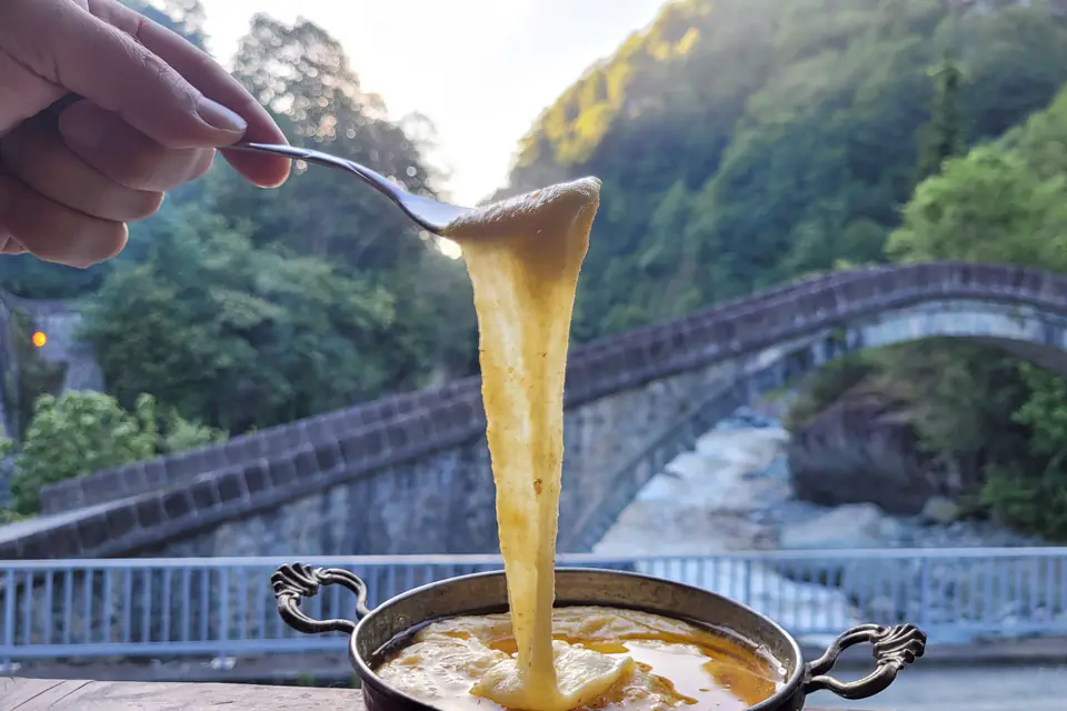 Stretchy cheese kuymak lifted with a spoon from a copper pan