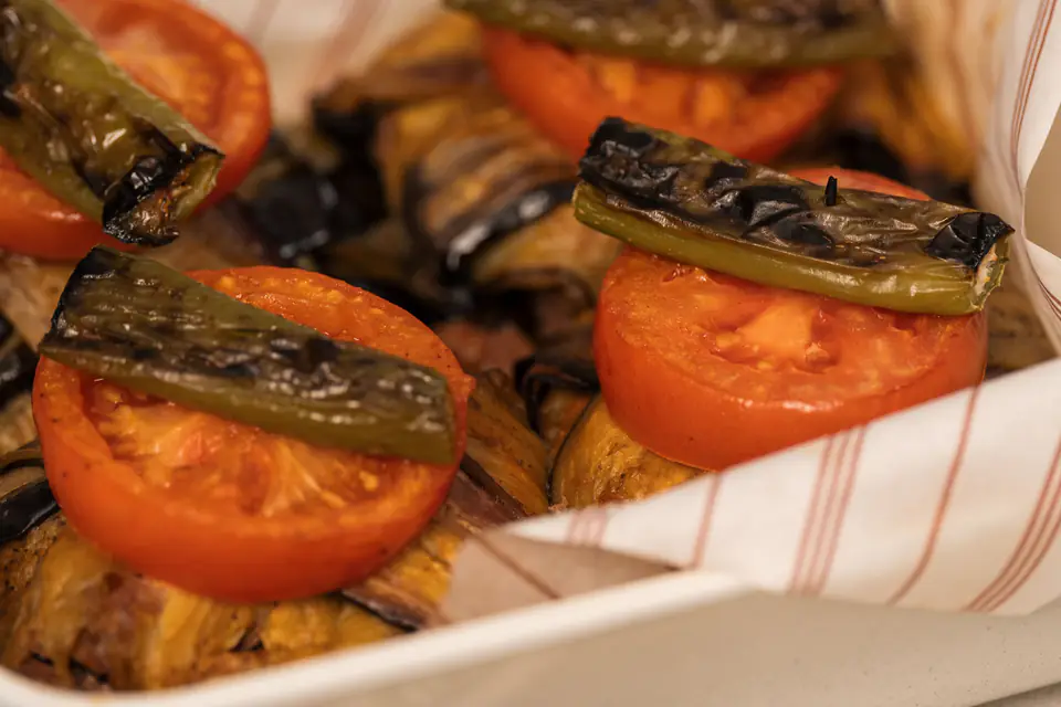 Eggplant kebab topped with tomatoes and roasted peppers in a baking dish