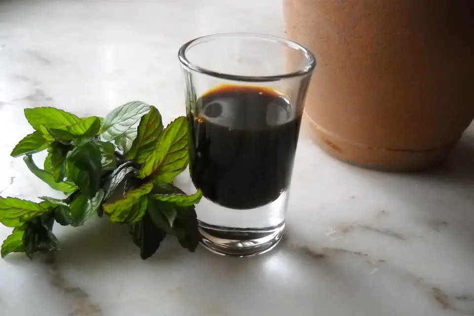 Dark grape molasses in a small glass with mint leaves
