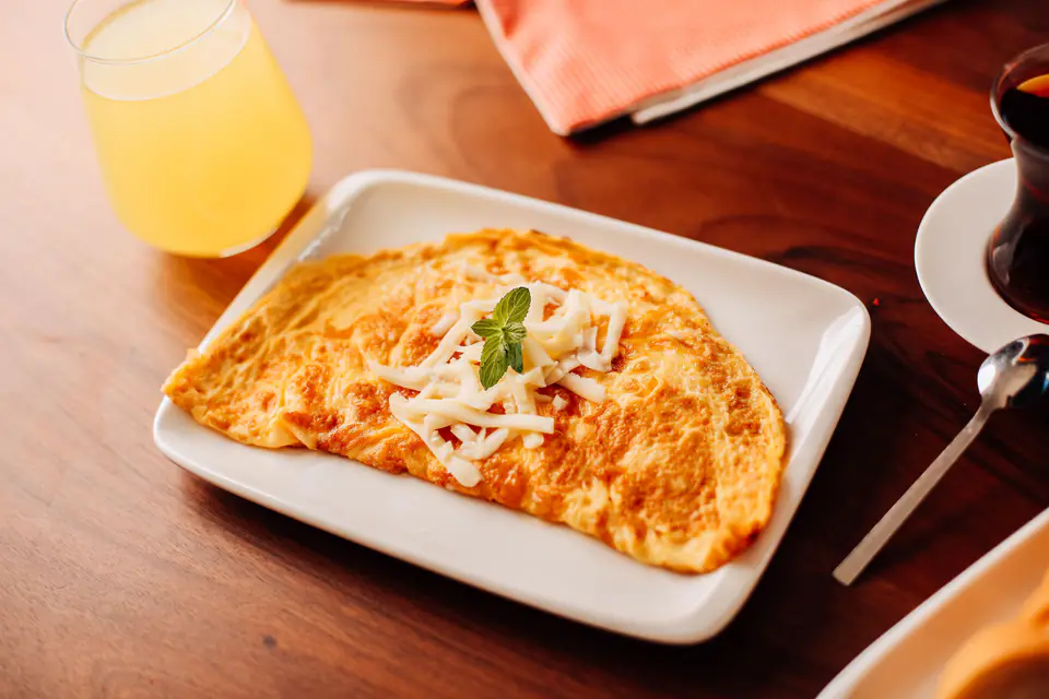 An omelette with grated cheese, juice and tea on the side