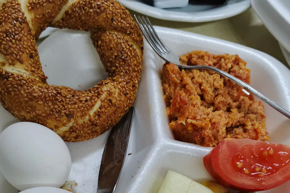 A simit with a boiled egg, cheese and tomatoes on a breakfast plate