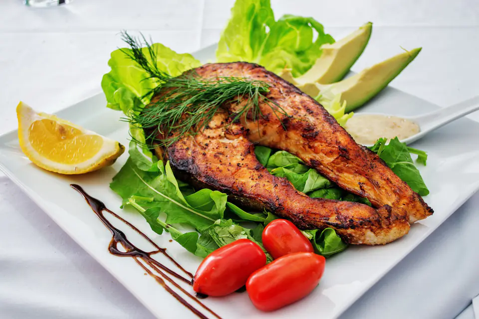 A grilled salmon fillet served with greens and tomatoes